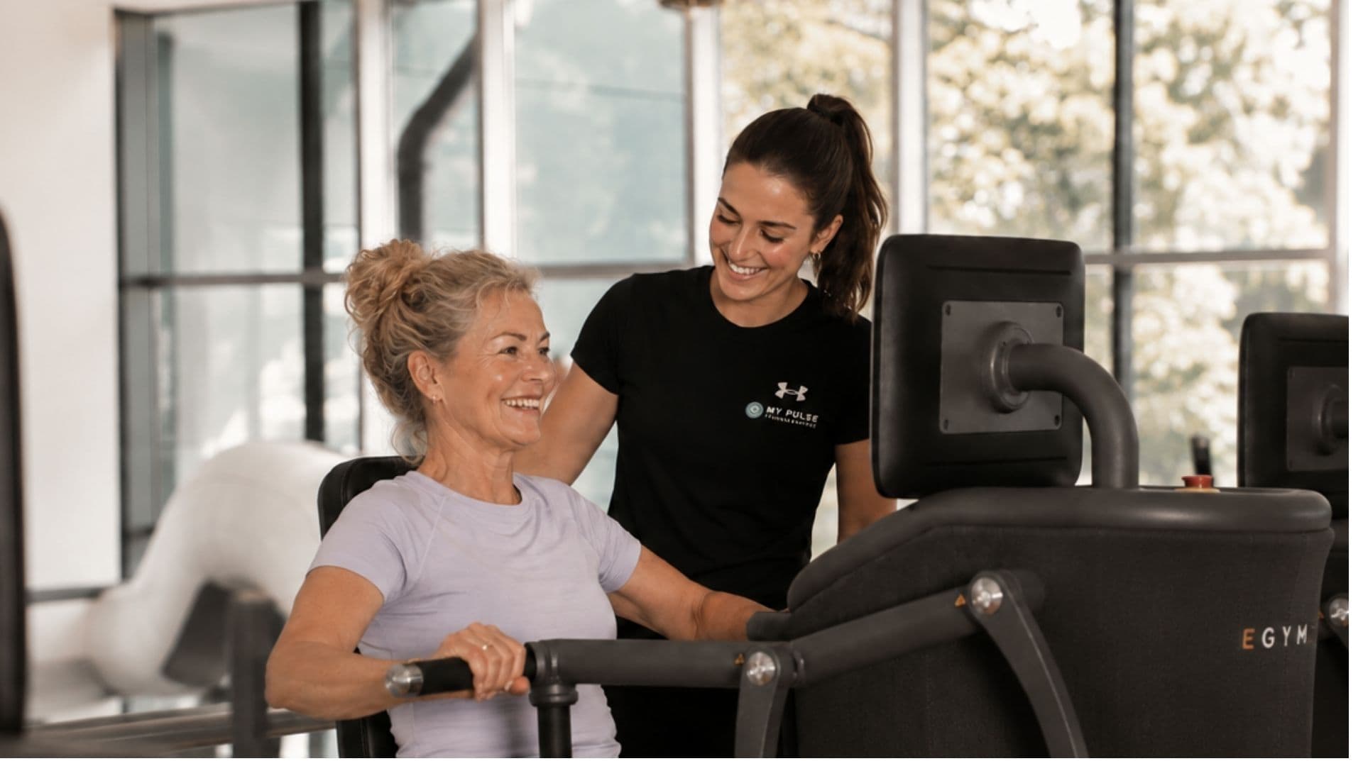 Mitglied trainiert an einem EGYM-Gerät, ein Trainer steht daneben