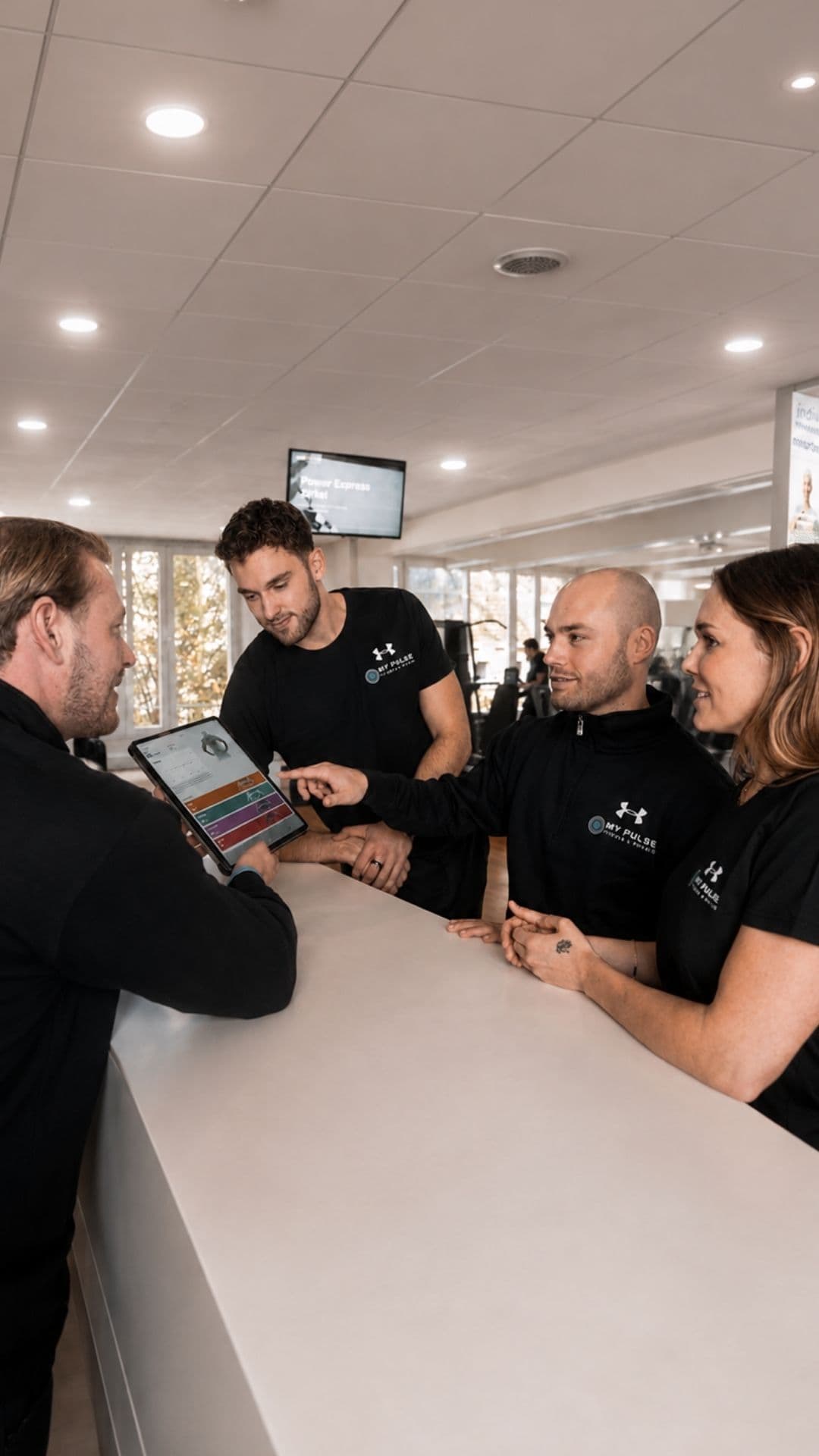 Vier Mitarbeitende von MY PULSE besprechen einen Trainingsplan am Tablet