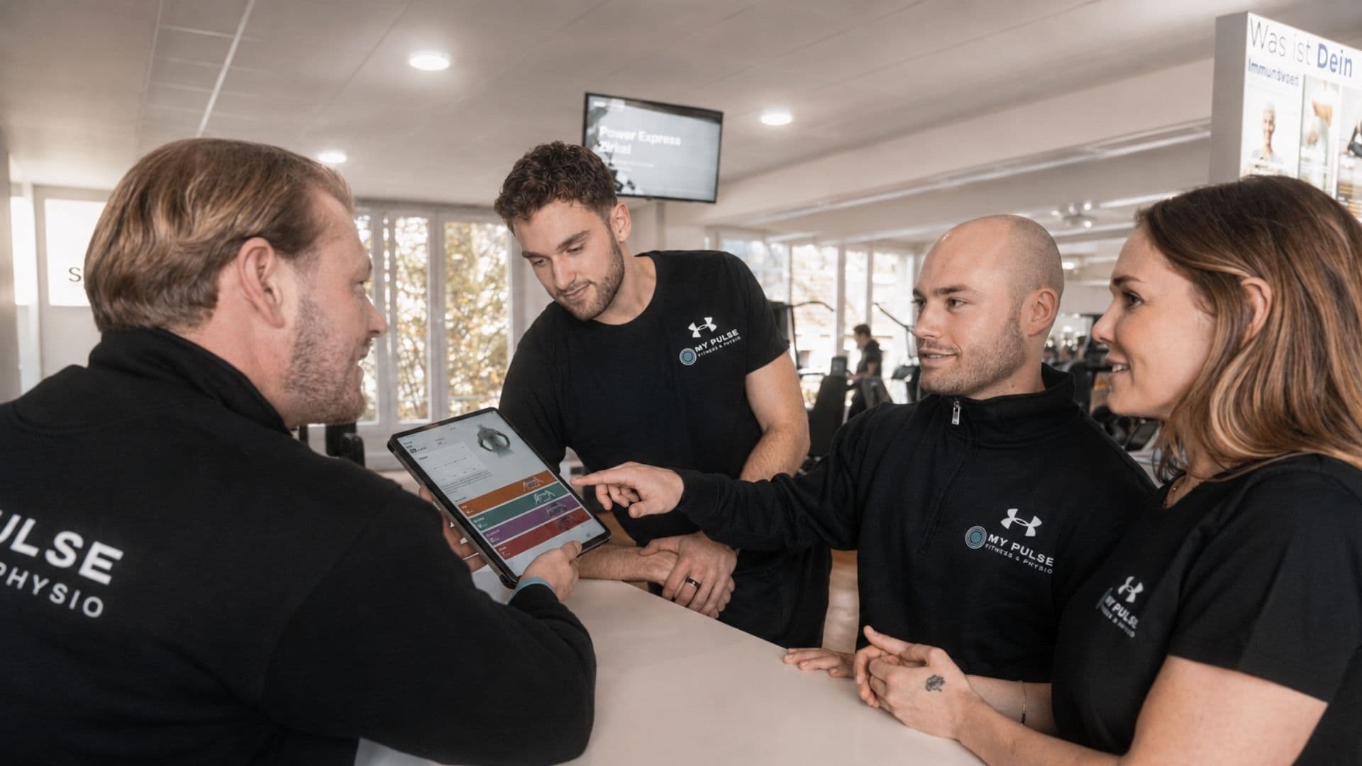Vier Mitarbeitende von MY PULSE besprechen einen Trainingsplan am Tablet