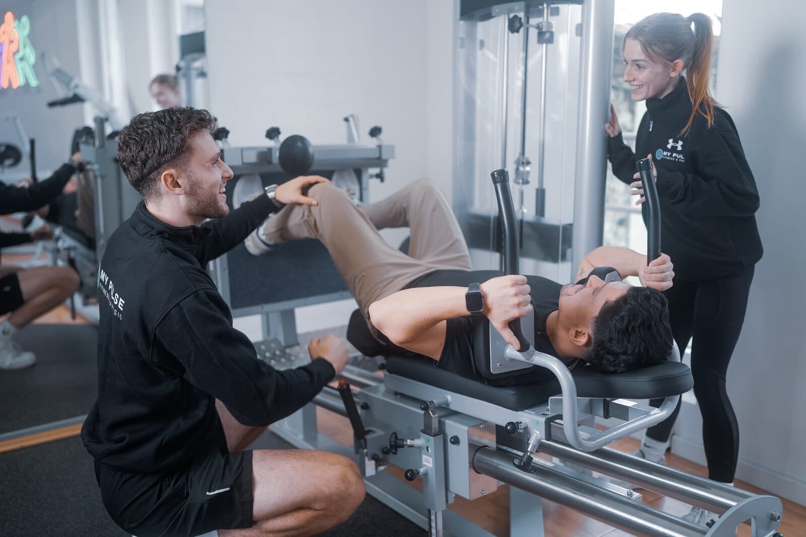 Trainer betreuen ein Mitglied gemeinsam am Gerät