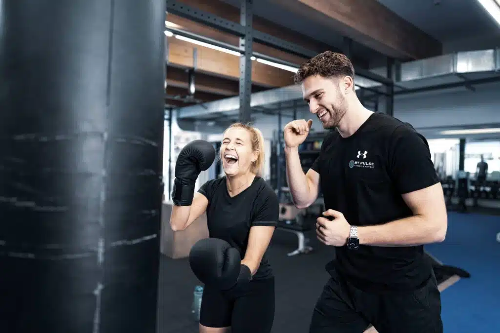 Personal Trainer begleitet Kundin beim Boxtraining am Boxsack im Gym